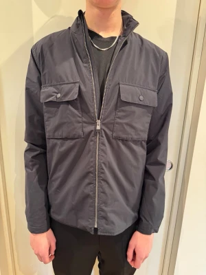 East West Jacka - Säljer en snygg blå East West jacka i färgen blå och storlek M. Modellen är 193 cm lång och väger 68 kg.