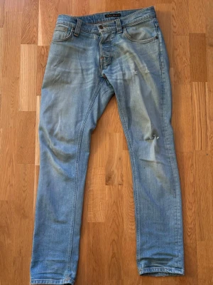 Ljusblå slim fit jeans från Nudie - Säljer ett par ljusblå slim fit jeans från Nudie. Jeansen har slitningar och en liten reva på ena benet för en avslappnad look. Perfekta till våren och sommarn.