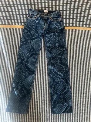 Blå jeans med ormmönster från Weekday - Säljer ett par blå jeans från Weekday med unikt ormmönster över hela byxan. Modellen har raka ben, klassisk femficksdesign och är gjorda i denim. Perfekta för dig som vill sticka ut med en cool och trendig look.