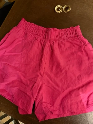 Rosa linneshorts från H&M - Säljer ett par snygga rosa shorts från H&M i linnemix. De har hög midja med resår och en loose passform som ger en avslappnad vibe. Perfekta för varma dagar! 