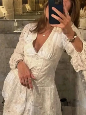 Zara viral slutsåld student klänning  - Söt vit kortklänning med v-ringning och långa ärmar. Klänningen har fina spetsdetaljer och broderade mönster i tyget. Tillverkad i bomull, perfekt för sommarens alla tillfällen. Luftig och feminin passform. 