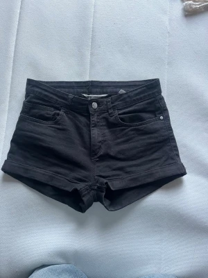 Svarta denimshorts med normal passform - Snygga svarta shorts i denim med klassisk femficksdesign och uppvikta benslut. Perfekta för varma dagar och enkla att matcha med olika stilar. Stängs med knapp och dragkedja framtill. Passar dig som gillar en enkel och clean look.