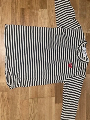 Randig långärmad topp Comme des Garçons - För dig som söker svalhet och stil under somman säljer en svartvit randig långärmad topp från Comme des Garçons PLAY med det ikoniska röda hjärtat på bröstet. Klassisk passform och rund halsringning. Perfekt för dig som gillar streetstyle och vill ha något tidlöst och trendigt i garderoben.            !!OBS FÖR FRÅGOR OM KVITTON ELLER ANNAT KONTAKTA MIG!!