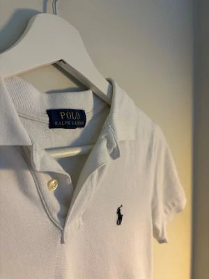 Vit polotopp från Ralph Lauren - Klassisk vit pikétröja från Ralph Lauren. Passar mellan 150 till 162 cm. Har en defekt på tröjan men inget som syns när man har på den. 