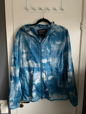 Blåvit vindjacka från Woolrich - Snygg blåvit vindjacka från Woolrich med molnliknande mönster. Jackan har huva, dragkedja framtill och är tillverkad i ett lätt, vindtätt material. Perfekt för dig som vill sticka ut med en unik look och samtidigt hålla dig skyddad mot vinden. Vid frågor så är det bara att skriva mvh William :)