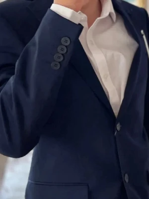 Mörkblå kostym  - Säljer en stilren mörkblå kostym med matchande kavaj och byxor. Kavajen har klassisk passform, knappar framtill och fickor. Perfekt för formella tillfällen. Använd 1 gång.  Kavaj Stl. 46,Regular, slim fit. Byxa stl. 31/30 slim fit. Kemtvättad efter användning.