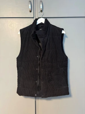 Mötkblå manchesterväst - Snygg mörkblå vadderad väst i manchester med hög krage och tryckknappar framtill. Västen har två fickor på sidorna och en quiltad look som ger extra stilpoäng. Perfekt att slänga över en hoodie eller tröja för en cool lager-på-lager stil. Perfekt nu på våren och kommande sommaren!