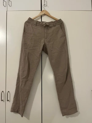 Beiga linnebyxor med dragsko - Snygga brun-beiga linnebyxor med avslappnad passform och dragsko, knapp och snörning i midjan. Byxorna har raka ben och sidofickor, perfekta för en chill och stilren look. Materialet är lätt och luftigt linne, vilket gör dem sköna att bära under varma dagar. 55% linne och 45% bomull. Storleken är M, mellan 30 och 35 i midjemått. Har inte använt linnebyxorna alls (på bilden ja). Det är bra kvalité och dem kostar runt 899 - 999 vanligtvis. 