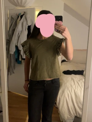 Olivgrön topp med volangärmar - Säljer en olivgrön topp i bomull med volangdetaljer på ärmarna. Modellen är croppad och har rund halsringning. Perfekt till jeans eller kjol😽