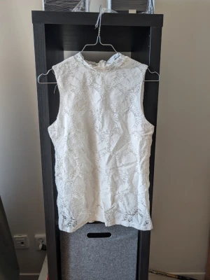 Vit spetsblus från Stockh LM - Säljer en elegant vit blus från Stockh LM i storlek S. Blusen är ärmlös och har vacker spets över hela plagget samt en hög hals. Dragkedja finns i nacken för enkel påklädning. Perfekt för dig som gillar en romantisk och stilren look.