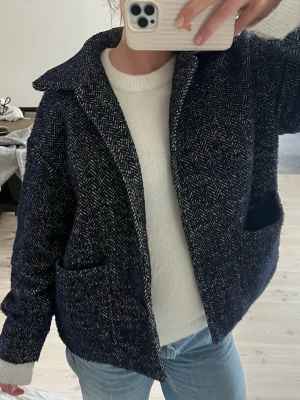 Mörkblå ullrock med fiskbensmönster - Snygg mörkblå rock i ullmix med klassiskt fiskbensmönster. Modellen har bred krage, stora framfickor och rak passform. Perfekt för dig som gillar en tidlös och trendig look.