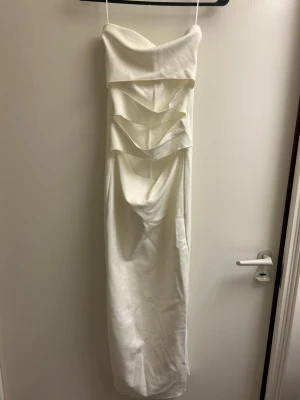 Vit långklänning från Zara med cut-outs - Trendig vit långklänning från Zara med tunna axelband och flera snygga cut-outs framtill. Klänningen har en figurnära passform och är perfekt för dig som vill sticka ut. Tillverkad i ett mjukt material som ger en lyxig känsla.