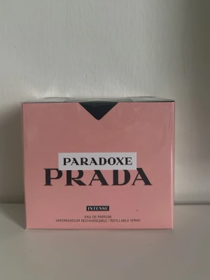 Prada Paradoxe Intense parfym - Prada Paradoxe Intense är en exklusiv parfym i en elegant rosa förpackning med svart och vit text. Doften är Eau de Parfum och flaskan är påfyllningsbar. Förpackningen har en modern och stilren design som känns lyxig och trendig.