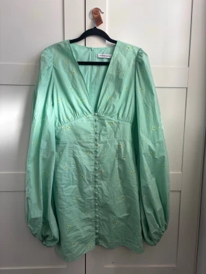 Mintgrön klänning från Adoore - Superfin mintgrön kortklänning från Adoore med v-ringning, långa puffärmar och små broderade blommor. Klänningen har knappar framtill och är tillverkad i ett lätt bomullstyg. Perfekt för vår och sommar!                                           Den har en knapp som är borta, därav priset, men man kan maila till adoore och få en ny😊