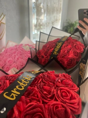 Bukett med konstgjorda rosor - Säljer en bukett med röda konstgjorda rosor, dekorerad med ett svart band där det står 'Grattis' i guldtext. Rosorna är tätt packade och ger ett lyxigt intryck, perfekt som present eller dekoration.