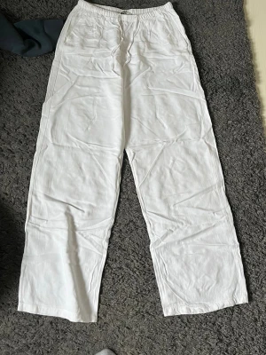 Vita linnebyxor från Gina Tricot XS - Säljer ett par vita linnebyxor från Gina Tricot i storlek XS. Byxorna har resår i midjan och raka ben för en avslappnad look. Tillverkade i ett lätt och luftigt linnematerial som passar perfekt till sommaren.