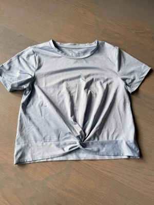 Ljusblå t-shirt med knutdetalj - Snygg ljusblå t-shirt i bomull med korta ärmar och rund halsringning. Framtill finns en trendig knutdetalj som ger en extra touch till looken. Perfekt till jeans eller kjol för en avslappnad stil.