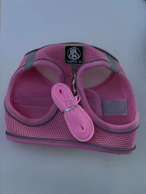 Rosa sele och koppel till husdjur - Säljer en rosa sele och matchande koppel från Together . Selen är tillverkad i meshmaterial med reflexdetaljer och har en söt hundlogga framtill. Passar smådjur som hund eller katt. Enkel att justera och stänga med kardborre och spänne. Storlek xs