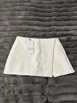 Kostym kjol från Zara - Asymmetrisk kostym skorts (shorts inuti kjol) från Zara. Storlek M, ny med prislapp. Crémefärgad