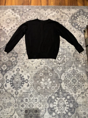 Svart basic sweatshirt - En enkel svart sweatshirt med rund hals och långa ärmar. Tröjan har ribbade muddar vid ärmslut och nederkant. Perfekt för en clean och avslappnad stil.
