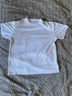 Vit basic t-shirt i polyester - En enkel vit t-shirt i 100% polyester med rund hals och korta ärmar. Perfekt för dig som gillar en clean och stilren look. Passar till allt och är superlätt att matcha med andra plagg. En liten skada (se på sista bilden)