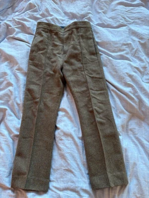 Bruna ullkostymbyxor Acne Studios  - Snygga kostymbyxor i brunmelerad ull med klassiskt pressveck och rak passform. Materialet är tjockt och ger en vintagekänsla. Perfekta för dig som gillar en stilren och tidlös look. Inga synliga fickor eller detaljer framtill.