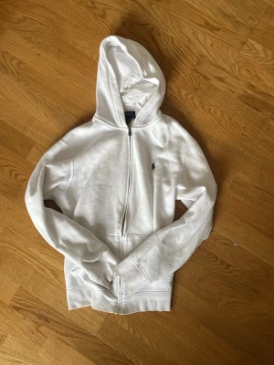 Vit hoodie från Polo Ralph Lauren (storlek S) - Säljer en clean vit hoodie från Polo Ralph Lauren med dragkedja och huva. Klassisk liten svart logga på bröstet. 