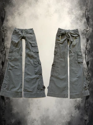 vida cargobyxor med fickor - Säljer ett par grå/gröna cargobyxor med stora fickor på sidorna. Byxorna har mycket detaljer och sömmar. Perfekta för en avslappnad och trendig streetwear-look.