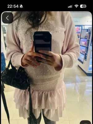 Ljusrosa stickad tröja med pärlor - Supersöt ljusrosa stickad tröja med pärlor och en stor stjärna framtill. Tröjan har långa ärmar, ribbade muddar och en lös passform. Perfekt att styla med kjol eller jeans för en trendig look.