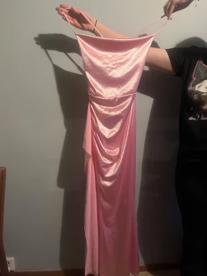 Lång rosa balklänning  - Säljer en lång, rosa klänning i satin med smala axelband och draperad detalj framtill. Klänningen har en figurnära passform, ”slit” vid höger ben och släpper snyggt längs kroppen. Perfekt för balen🙏🏻🫶🏻