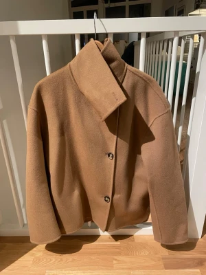 Kamelbrun ullkappa  - Stilren kamelbrun kappa i 100% ull med rak passform. Perfekt för kyliga dagar när du vill vara både varm och snygg. Nypris 2500 kr. Sparsamt använd. Storlek 36 men är rymlig och passar även en 38.