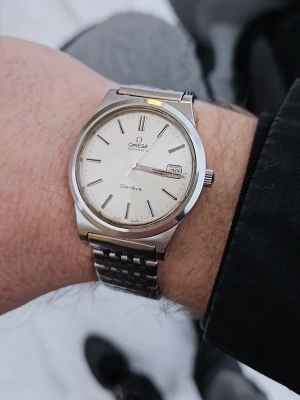 Omega Genève Automatic herrklocka  - Omega Genève Automatic (1974). Klockan är i originalskick. Specifikationer: Referens: 166.0168 Årtal: 1974 Storlek: 38mm (exkl. kronan).  Information: Länken har förlängts med en extra bit av en urmakare för att passa en större handled (se bilden). Denna kan enkelt tas bort för en smalare passform. Klockan säljs i befintligt skick då den inte servats I min ägo. Den fungerar vid användning men kronan är trög och gångreserven är för tillfället kort. En service rekommenderas. Omega lådor medföljer.