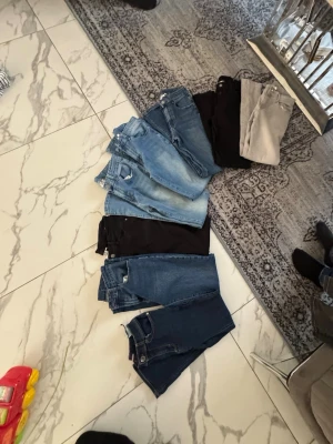 Jeanspaket i olika färger - Säljer ett paket med flera par jeans i olika färger, från ljusblått till mörkblått, svart och grått. Klassisk femficksmodell och raka ben. Perfekt för dig som vill ha variation i garderoben. Inget synligt märke eller material framgår.