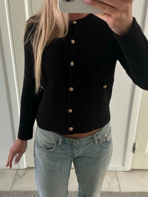 Svart kofta med guldknappar - svart kofta med långa ärmar och dekorativa guldknappar framtill. 