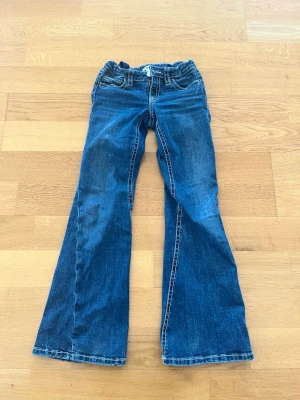 Blå bootcut jeans med mönstrade fickor - Säljer ett par blå bootcut jeans med snygga broderade bakfickor och silvriga knappar. Ursprungligen från Gina tricot💕