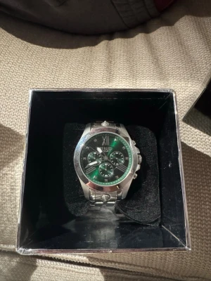 Versus Versace silverfärgad klocka - Snygg klocka från Versus Versace med silverfärgat armband och boett. Urtavlan är grön med flera mindre visare och romerska siffror upptill. Aldrig använd .