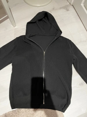 Stickad hoodie  - Säljer en svart stickad hoodie med dragkedja framtill. Hoodien har en stor huva och ribbade muddar vid ärmslut och nederkant. Perfekt för dig som gillar en enkel och stilren look. Materialet är mjukt och ger en skön känsla. Storlek XXS men sitter ungefär som XS