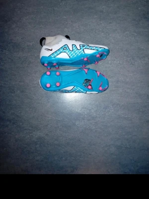 Nike Air Zoom vita/blå fotbollsskor - Säljer ett par Nike Air Zoom fotbollsskor i vitt och blått med rosa dobbar. Skorna har en högre strumpliknande krage och stor svart Nike-logga på sidan. Snygg design med mönstrade detaljer och slitstark syntetisk ovandel. Perfekta för dig som vill sticka ut på planen.