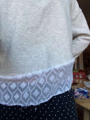 Grå tjocktröja med spetsdetalj - Säljer en ljusgrå tjocktröja med bred vit spetskant nertill. Tröjan har en avslappnad passform och långa ärmar. Spetsen har ett geometriskt mönster som ger en unik touch. Perfekt för dig som gillar att mixa basic med något extra. Tröjan är ursprungligen från lager 157, men spetsen har jag själv sytt dit och den sydde jag lite snett för att få en modern/cool känsla❣️buda gärna🤗