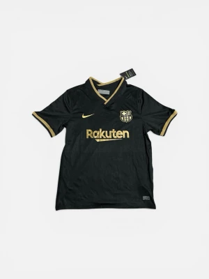 Svart FC Barcelona matchtröja - Snygg svart FC Barcelona matchtröja från Nike med guldfärgade detaljer och loggor. Tröjan har korta ärmar, V-ringning och tryck från Rakuten och UNICEF. Tillverkad i ett lätt och funktionellt material som passar perfekt till träning eller match.