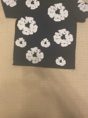 Mörkblå t-shirt med vita blommor (denim tears) - Snygg svart t-shirt från denim tears med stora vita blommönster över hela tröjan. T-shirten har klassisk passform och rund hals. Perfekt för dig som vill sticka ut med ett coolt och trendigt mönster. Materialet känns mjukt och bekvämt mot huden. (ALDRIG ANVÄND) priset kan diskuteras