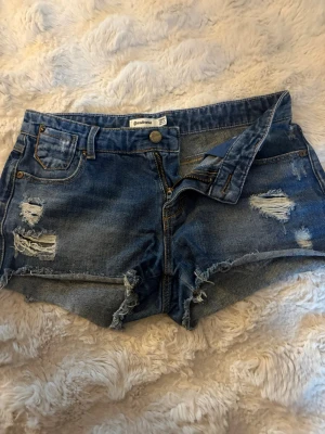 Mörkblå jeanskjol med slitna detaljer  - Säljer ett par blå jeansshorts med slitna detaljer och fransig kant. I passformen är de ganska korta och lågmidjade!💗💗De är i storlek 34 och är ifrån stradivarius.