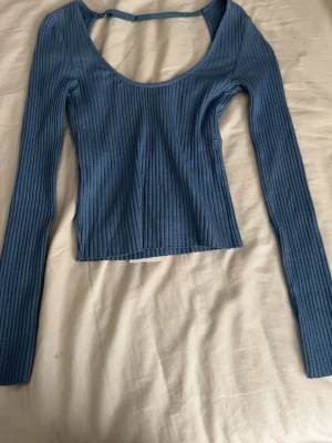 Blå ribbad topp från Zara - Trendig blå ribbad topp från Zara med lång ärm och djup rundringning och öppen rygg. Toppen har en croppad passform och är tillverkad i mjuk, stretchig bomullsmix. Perfekt för att styla med höga jeans eller kjol.