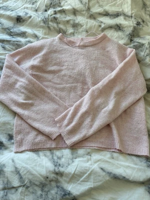 Ljusrosa stickad tröja - Mysig ljusrosa stickad tröja med rund hals och långa ärmar. Tröjan har ribbade muddar vid ärmslut och nederkant. Perfekt för lager på lager och enkel att matcha med jeans eller kjol. Materialet känns mjukt och behagligt mot huden.
