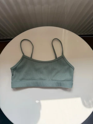 Grön ribbad bikini. - Stilren bikini i ljusgrönt ribbat tyg med tunna axelband och rak skärning. Materialet är stretchigt och bekvämt, perfekt för strandhäng eller poolen. Inga synliga loggor eller detaljer, bara enkel och clean design. I storlek 134/140. Från kappahl