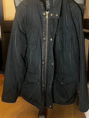 Svart snygg jacka från J.Lindbergh  - Säljer en svart utilityjacka från J.Lindbergh med flera praktiska fickor framtill, dragkedja och tryckknappar. Jackan har axelklaffar och quiltat foder på insidan. Perfekt för dig som gillar streetwear och funktionella detaljer.nyåros 4400kr mitt pris 1000kr