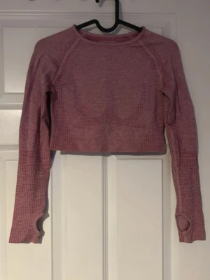 Träningströja  - Croppad långärmad träningströja i rosa melerad färg. Tröjan har tumhål i ärmsluten och en bekväm passform. Perfekt för gym, yoga eller annan träning. (Minns inte vart jag köpte den)