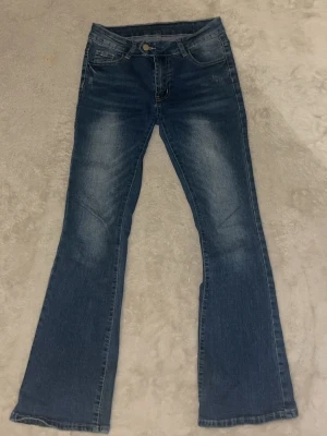 Blå bootcut jeans med slitningar - Snygga blå bootcut jeans med lätt slitna detaljer framtill och bakfickor. Jeansen har klassisk femficksdesign, normal midja och är gjorda i denim. Perfekta för dig som gillar en avslappnad men trendig look.