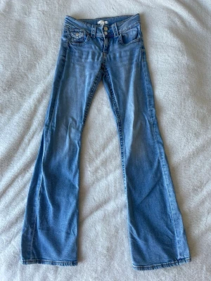 Ljusblå bootcut jeans med låg midja - Säljer ett par ljusblå bootcut jeans med låg midja och klassiska fem fickor. Jeansen har utsvängda ben och dubbla knappar i linningen. 