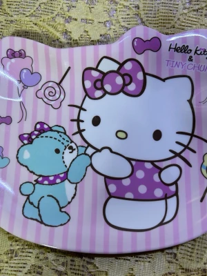 Hello Kitty barn tallrik  - Två fat i plast med Hello Kitty-motiv. Ena fatet har rosa och vita ränder med Hello Kitty och en blå björn, dekorerat med rosetter och godis. Det andra fatet är ljusrosa med hjärtan, jordgubbar och noter. Perfekta för snacks eller småsaker.  65kr/st , helt ny 
